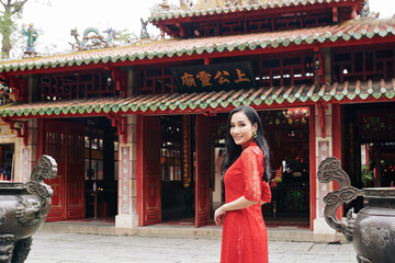 Poster - Beautiful young Asian woman in red lace dress standing at Buddhist temple and smiling at camera