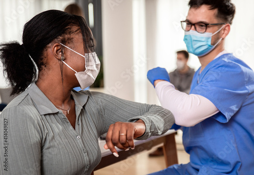 Male nurse with mask greeting with patient in clinic.