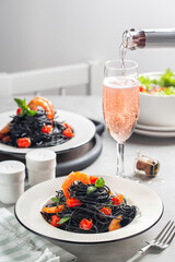 Wall Mural - Italian dinner. Squid ink spaghetti, with shrimp and cherry tomatoes and flowing rose wine. On white table.