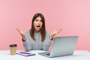 How could you? Shocked annoyed woman office worker raising hands in indignant gesture, asking why and looking angrily, sitting at workplace with laptop. Indoor studio shot isolated on pink background