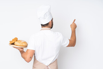 Wall Mural - Male baker holding a table with several breads isolated on white background pointing back with the index finger