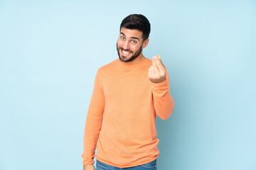 Caucasian handsome man making money gesture over isolated blue background