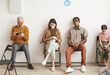 Full length portrait of multi ethnic group of people wearing masks and sitting in row on chairs while waiting in line at clinic, copy space