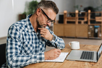 Wall Mural - Focused grey man writing down notes while working with laptop