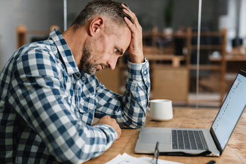 Wall Mural - Tired grey man working with laptop while sitting in office