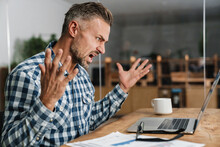 Furious Grey Man Screaming And Gesturing While Working With Laptop