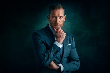 Wall Mural - Studio portrait of businessman looking deep in thought while standing at isolated dark background