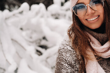 A girl in a sweater and glasses in winter in a snow-covered forest