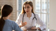 © fizkes - Focused young beautiful female doctor talking with woman at checkup meeting, explaining medical insurance benefits or fiving advice on health treatment procedures, sitting at table in clinic office.