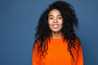 Smiling cheerful funny attractive young african american woman wearing casual basic bright orange sweatshirt posing standing and looking camera isolated on blue color background studio portrait.