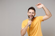 Young caucasian smiling bearded handsome student happy man 20s wear casual yellow basic t-shirt sing song in microphone enjoying leisure time dancing isolated on grey color background studio portrait.