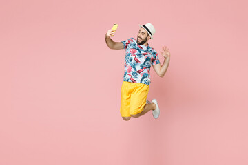 Wall Mural - Full length of cheerful traveler tourist man in summer clothes hat jumping doing selfie shot on mobile phone isolated on pink background. Passenger traveling on weekend. Air flight journey concept.