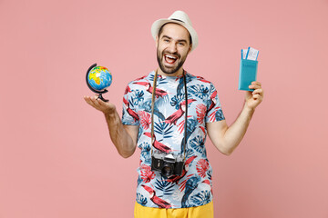 Canvas Print - Cheerful young traveler tourist man in summer clothes hat photo camera hold Earth world globe passport tickets isolated on pink background. Passenger traveling on weekend. Air flight journey concept.