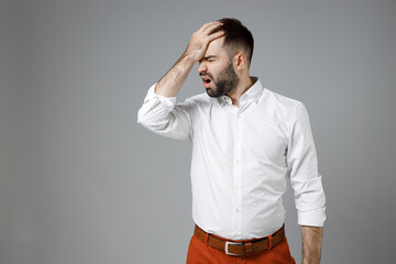 Displeased young bearded business man in classic white shirt standing put hand on face facepalm epic fail gesture isolated on grey color background studio portrait. Achievement career wealth concept.