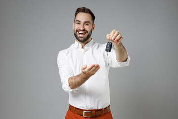 Wall Mural - Laughing cheerful funny young bearded business man 20s wearing classic white shirt stand pointing hand on car keys isolated on grey color background studio portrait. Achievement career wealth concept.