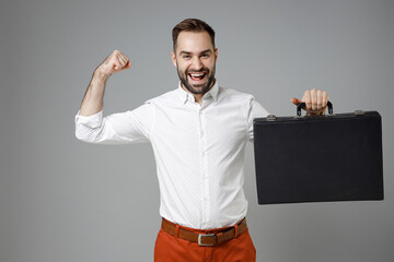 Strong funny young bearded business man 20s in classic white shirt hold briefcase showing biceps muscles on hand isolated on grey color background studio portrait. Achievement career wealth concept.