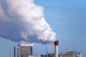 White smoke erupts from the chimney of the city's gas heating boiler house against the blue winter sky