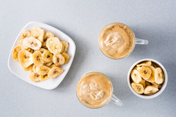 Quarantine trendy cuisine. Two cups with dalgona coffee and banana chips on a gray background. Top view