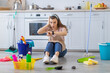 © Prostock-studio - Full length of terrified professional maid sitting on floor at kitchen with cleaning supplies, looking at her watch
