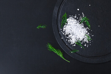 Wall Mural - Coarse salt crystals on a black table. Bowl with sea salt. Background for advertising salty.