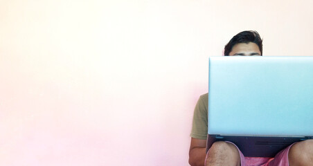 Poster - Male holding a laptop on his knees while sitting on a floor leaning against a white wall