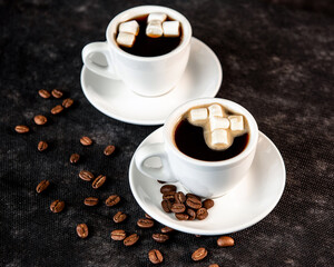 Coffee in white cups and small marshmallows. Turkish coffee, marshmallows on a dark background. Close-up. Two cups of coffee with marshmallows, coffee beans