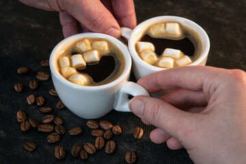 Wall Mural - Two cups of black coffee with a small marshmallow. Coffee in the hands of a man and a woman. Close-up