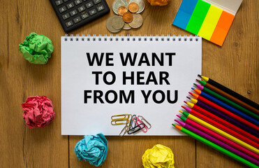Wall Mural - Support symbol. White note with words 'we want to hear from you' on beautiful wooden table, colored paper, colored pencils, paper clips, coins and calculator. Business and support concept.