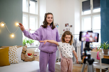 Wall Mural - Sisters indoors at home, making video with smartphone. Lockdown concept.