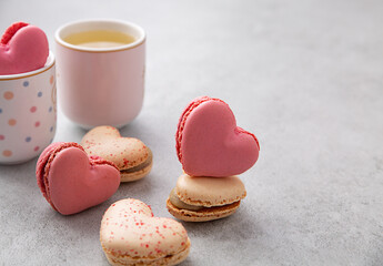 Macarons or French macaroons in heart shapes and two cups on gray background with copy space