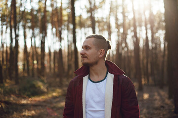 bearded guy with stylish hairstyle looks to the side in pine forest blurred background bokeh effect