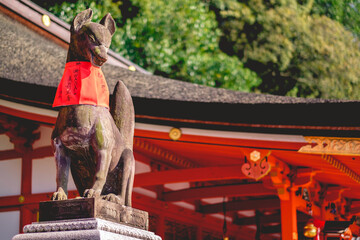 Fox (kitsune) stone statue wit red scarf at Fushimi Inari taisha shrine entrance stairs, Kyoto