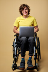 man disabled student preparing for exam using laptop, sitting on wheelchair isolated in studio. portrait. online education for handicapped people