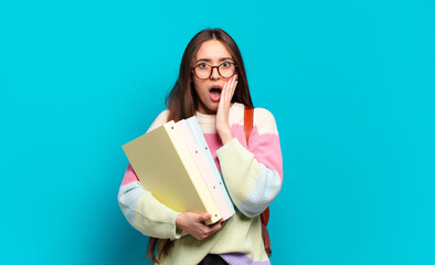 Wall Mural - young pretty woman feeling shocked and scared, looking terrified with open mouth and hands on cheeks