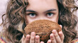 exotic summer close-up portrait of a beautiful girl with blue eyes and curly hair with a coconut in her hands