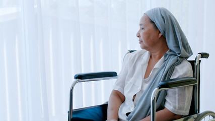 An elderly woman with cancer sitting in a wheelchair looking out of the window while being hospitalized.