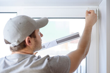 Man installing gray pleated blinds on the window