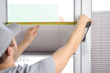 Man installing gray pleated blinds on the window