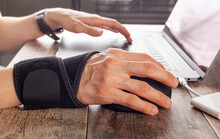 Chronic Trauma To The Wrist Joint  In People Using Computer Mouse May Lead To Disorders That Cause Inflammation And Pain. A Woman Working On Desk Uses Wrist Support Brace And Ergonomic Vertical Mouse