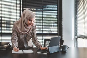 Wall Mural - Beautiful asian muslim business woman brown hijab sitting and working with laptop computer at modern office.