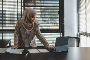 Wall Mural - Beautiful asian muslim business woman brown hijab sitting and working with laptop computer at modern office.