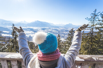 Happy young woman is raising her hands on the mountain, enjoying the view over Salzburg. Winter time on Gaisberg, Salzburg, Austria