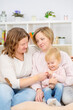 © Ermolaeva Olga - Two young women are sitting on the couch by the seyu at home in the living room and playing with their little daughter. Gay lesbian couple at home with a baby. Lesbian family