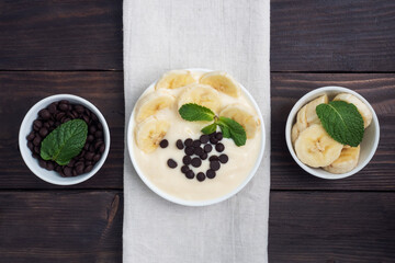 Wall Mural - Healthy breakfast, dessert with milk yogurt banana and chocolate on a plate. Dark wooden background. Top view