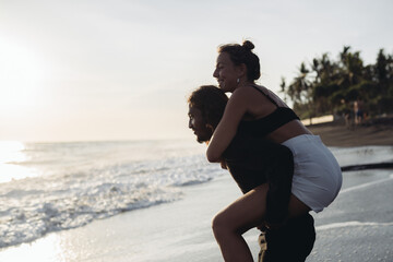 A man on the beach put a woman on his butt and they laughed at the ocean waters. High quality photo