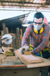 © anusak - carpenter is working in a woodworking office.caucasion white Carpenter using sandpaper to polish the wood and brush off the sawdust.