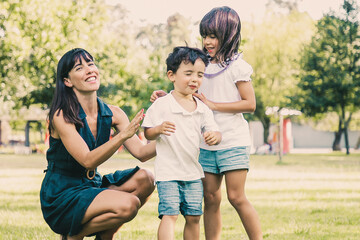 Two happy kids and their mom playing active games in park. Boy with closed eyes walking on grass lead by sister and mother. Family outdoor activity and leisure concept