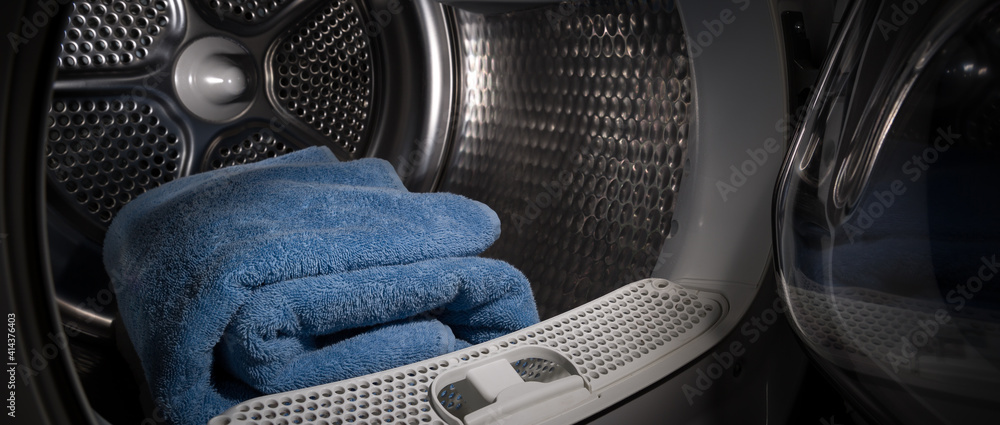 Dryer with open door in a dark room. Blue towels are stacked inside the drum.