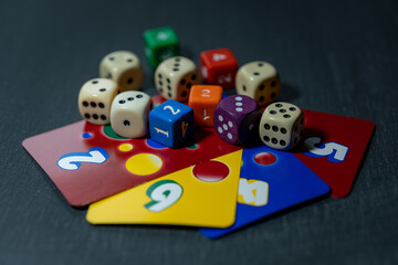 Colourful dice lie on colourful playing cards against a dark, neutral background.