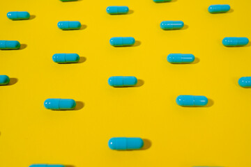 Wall Mural - Close up - Blue pills of same color lie on a yellow background. Macro photo. The concept of victory over the coronavirus or vaccination. The end of the pandemic.